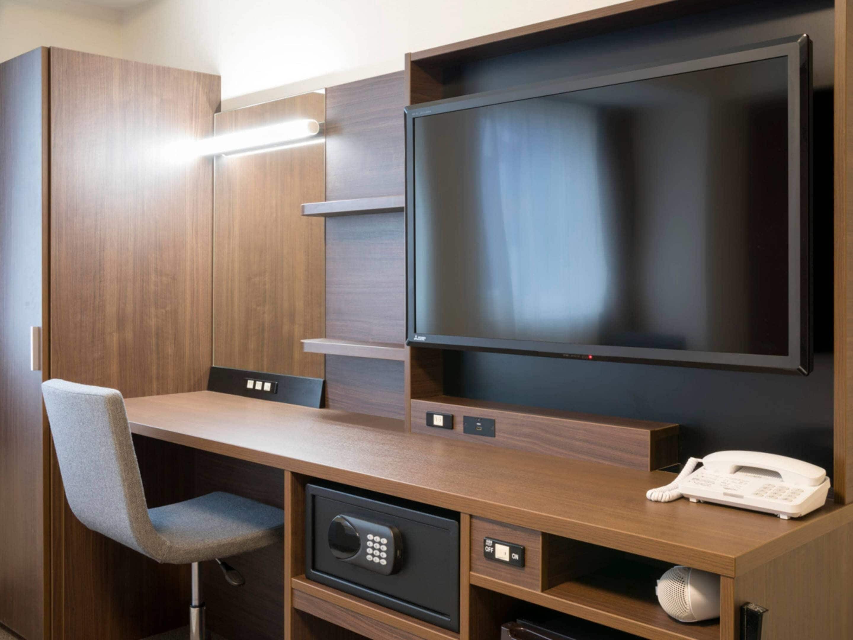 A hotel room with a wooden desk, a television, a telephone, and a safe.