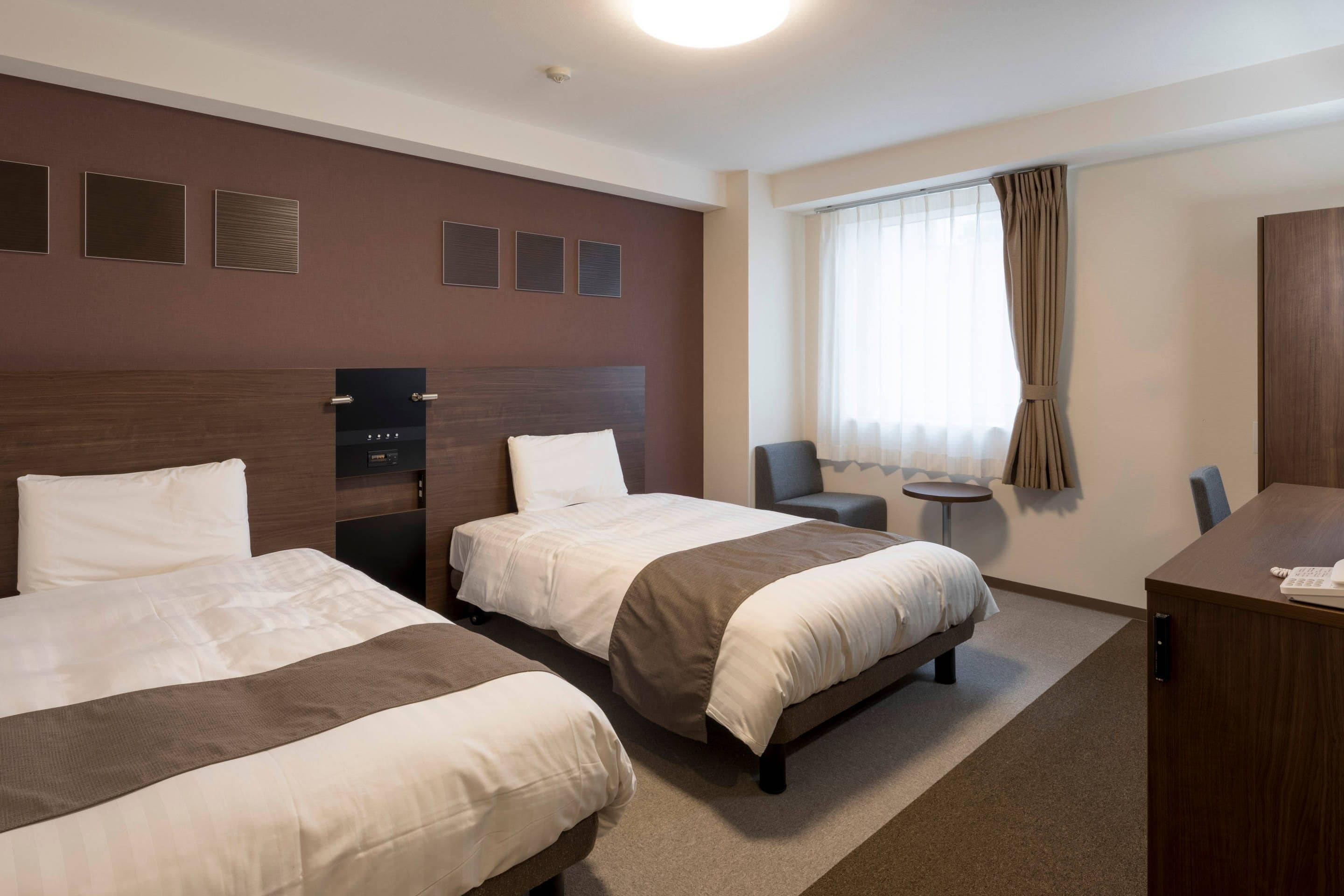 A hotel room with two beds, a desk, a chair, and a window with curtains.
