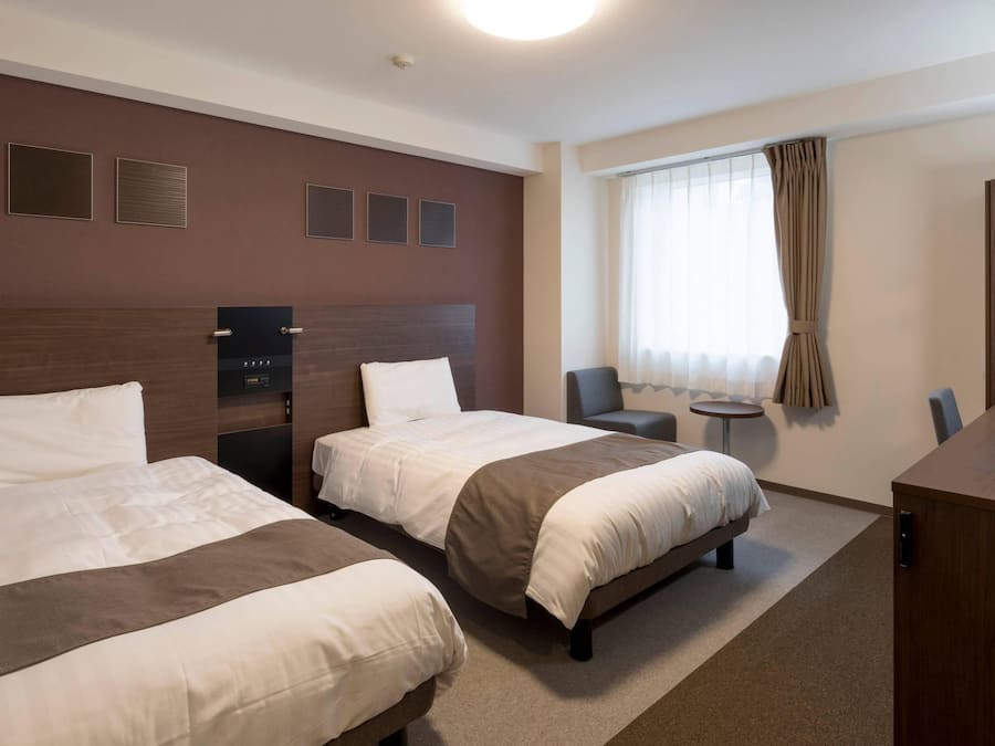 A hotel room with two beds, a desk, a chair, and a window with curtains.