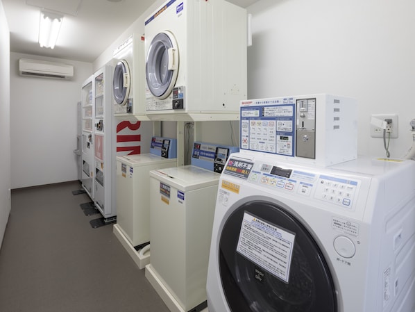 A laundry facility with multiple washing machines and dryers, control panels, and a fire extinguisher.