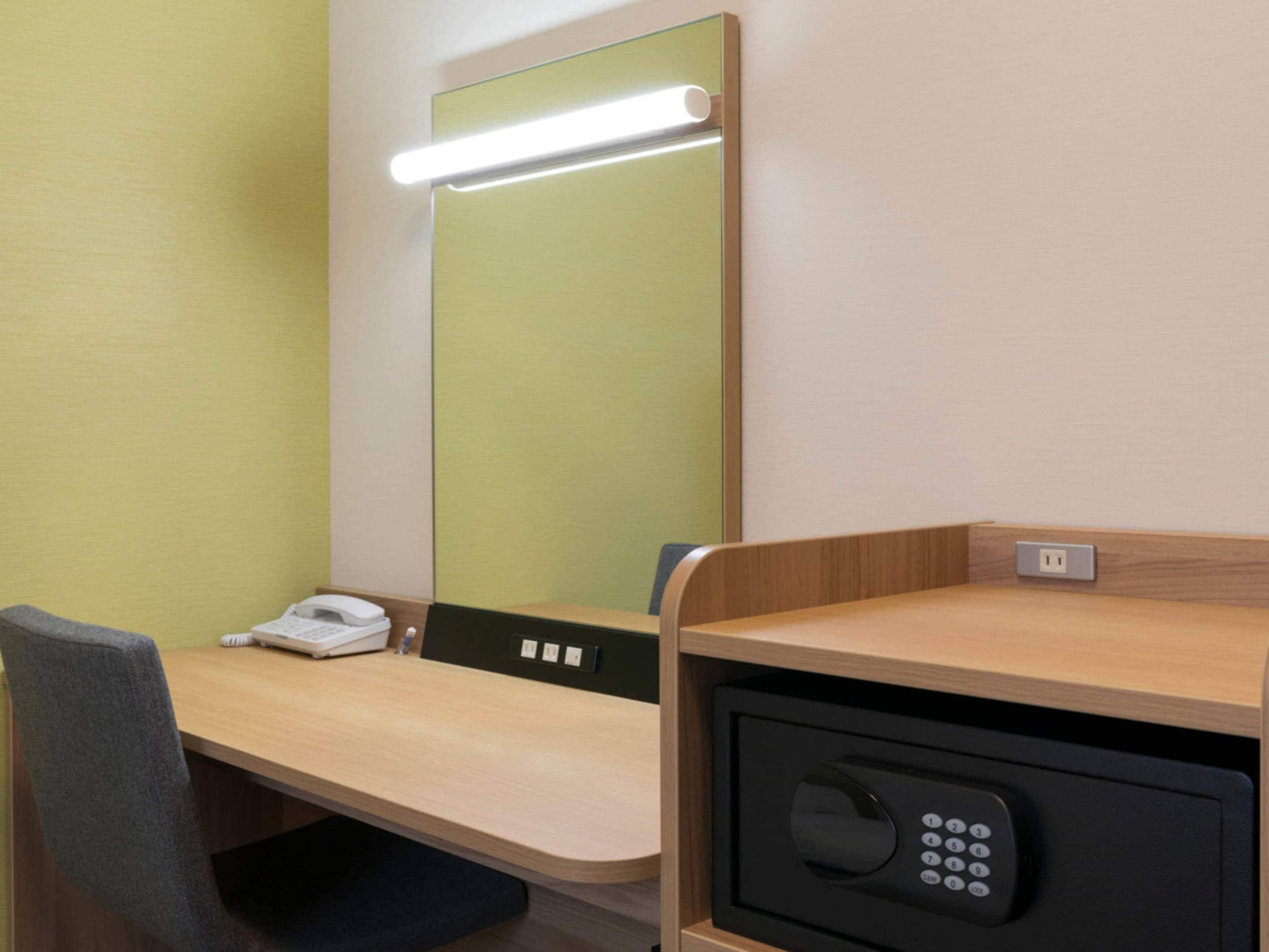 Una habitación de hotel con escritorio, teléfono, espejo y caja fuerte.