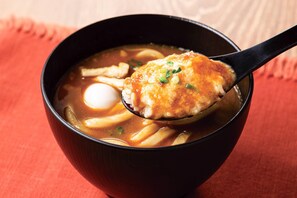 A bowl of ramen with a spoon lifting a piece of meat and a boiled egg. - Comfort Hotel Toyohashi (Toyohashi)
