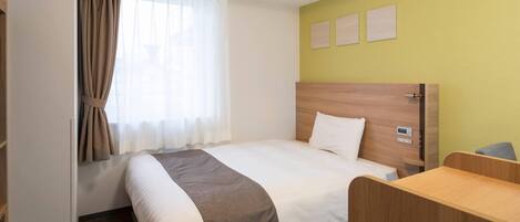 Una habitación de hotel con cama, escritorio, ventana con cortinas y una pared con tres cuadros.