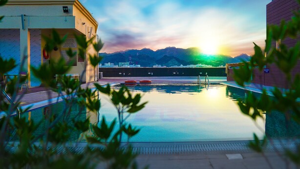 A swimming pool with a view of mountains and a sunset. - Golden Tulip Headington Ruwi (Muscat)