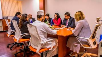 A conference room with a wooden table, white chairs, and a meeting in progress.
