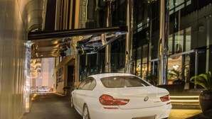 A white BMW parked in front of a modern building with large arched windows and a reflective facade. - Golden Tulip Headington Ruwi (Muscat)