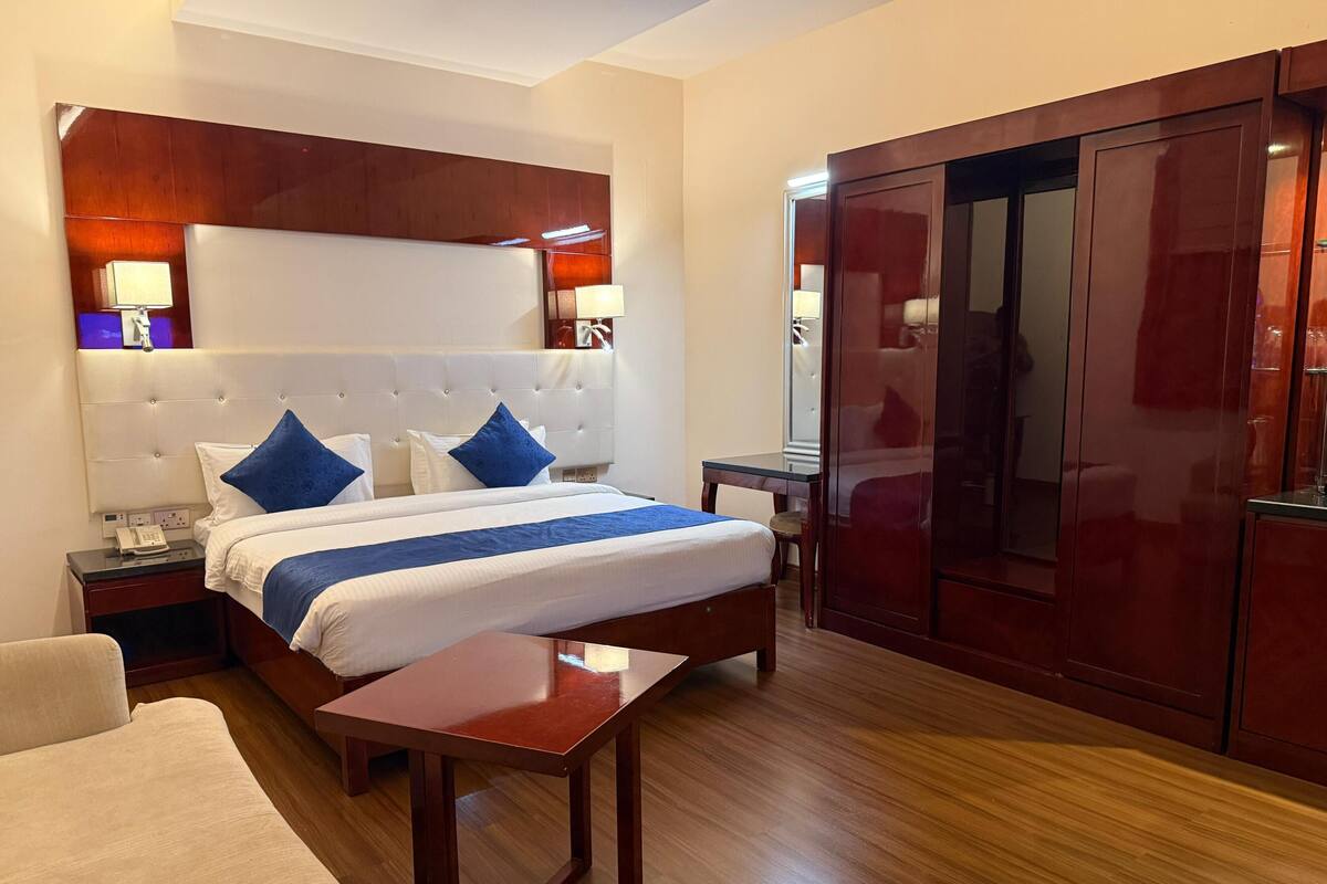 A hotel room with a large bed, a wooden headboard, a desk, and a wardrobe.