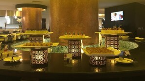 A buffet setup with multiple food stations, a television screen, and decorative lighting. - Golden Tulip Headington Ruwi (Muscat)