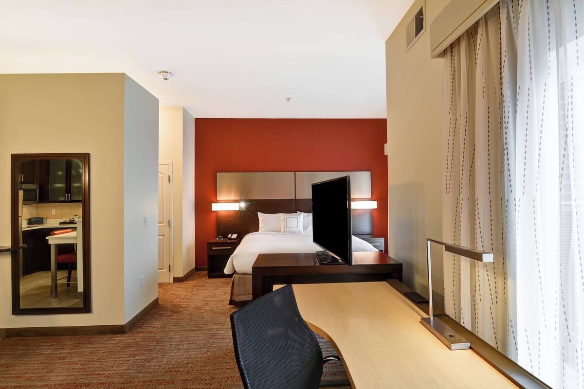 A hotel room with a bed, bedside table, chair, desk, and a mirror.
