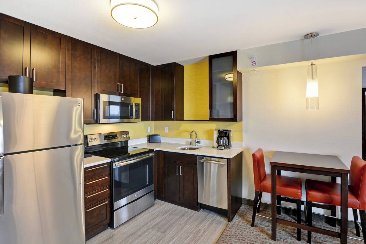 A compact kitchen with a refrigerator, stove, microwave, and dishwasher. There is a small dining area with a table and two chairs.