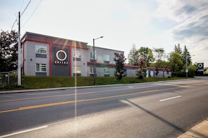 A modern hotel building with a prominent circular logo on the facade, a well-maintained lawn, and a clear road in front.