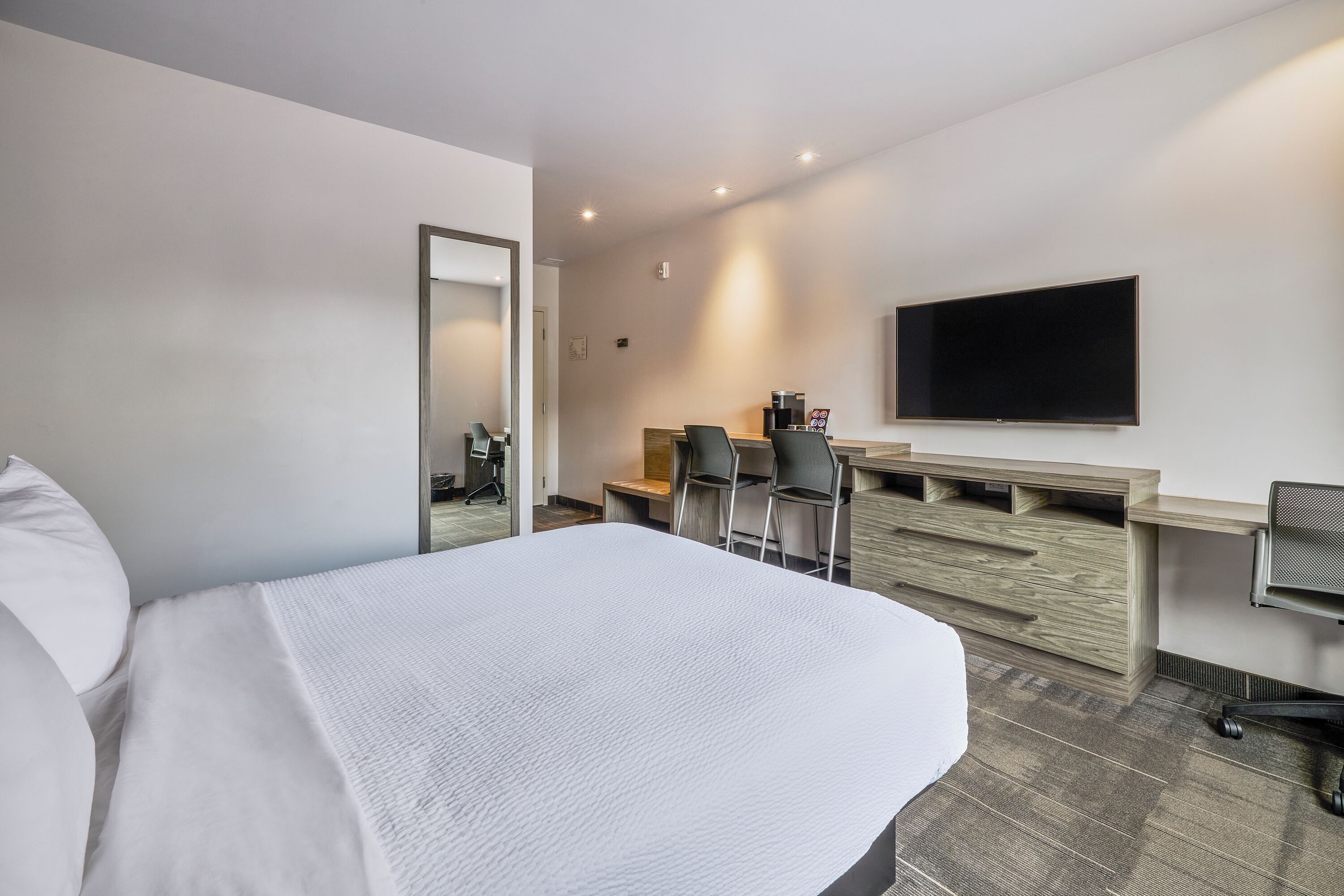 Een hotelkamer met een bed, een bureau met stoel, een televisie en een spiegel.