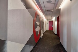 Un pasillo con un diseño geométrico en la pared, una puerta roja al final y suelo alfombrado.