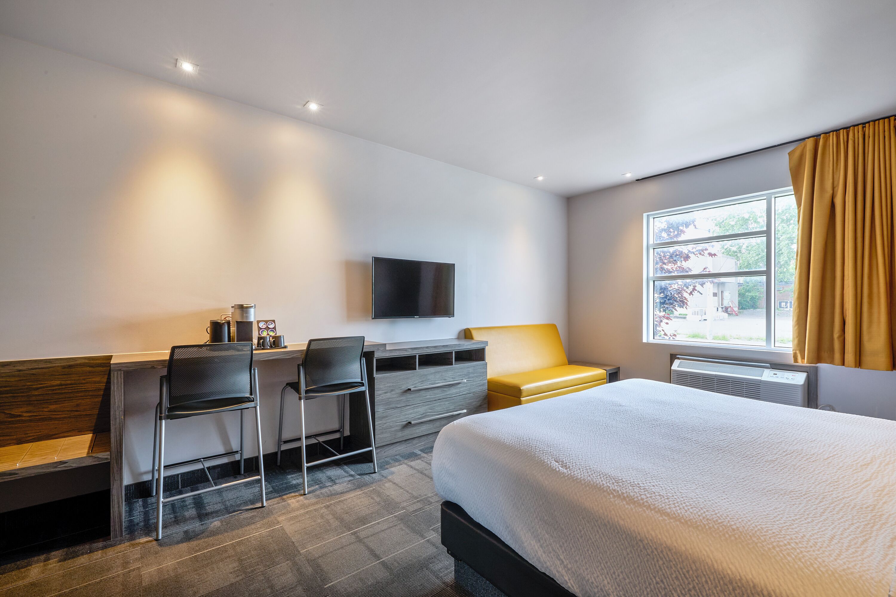 A hotel room with a bed, desk, two chairs, a flat-screen TV, and a window with curtains.
