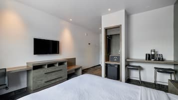 Habitación de hotel moderna con una cama grande, un televisor de pantalla plana montado en la pared, un escritorio integrado con una silla, un refrigerador pequeño y una cafetera.