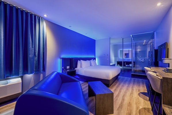 A modern hotel room with a bed, a desk, a chair, and a sofa.