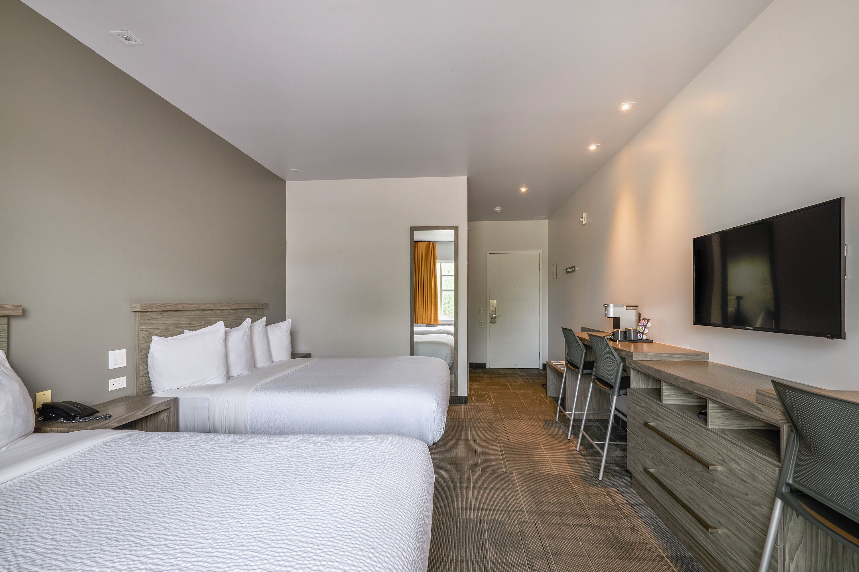 A hotel room with two beds, a desk with a chair, a flat-screen TV, and a coffee machine.