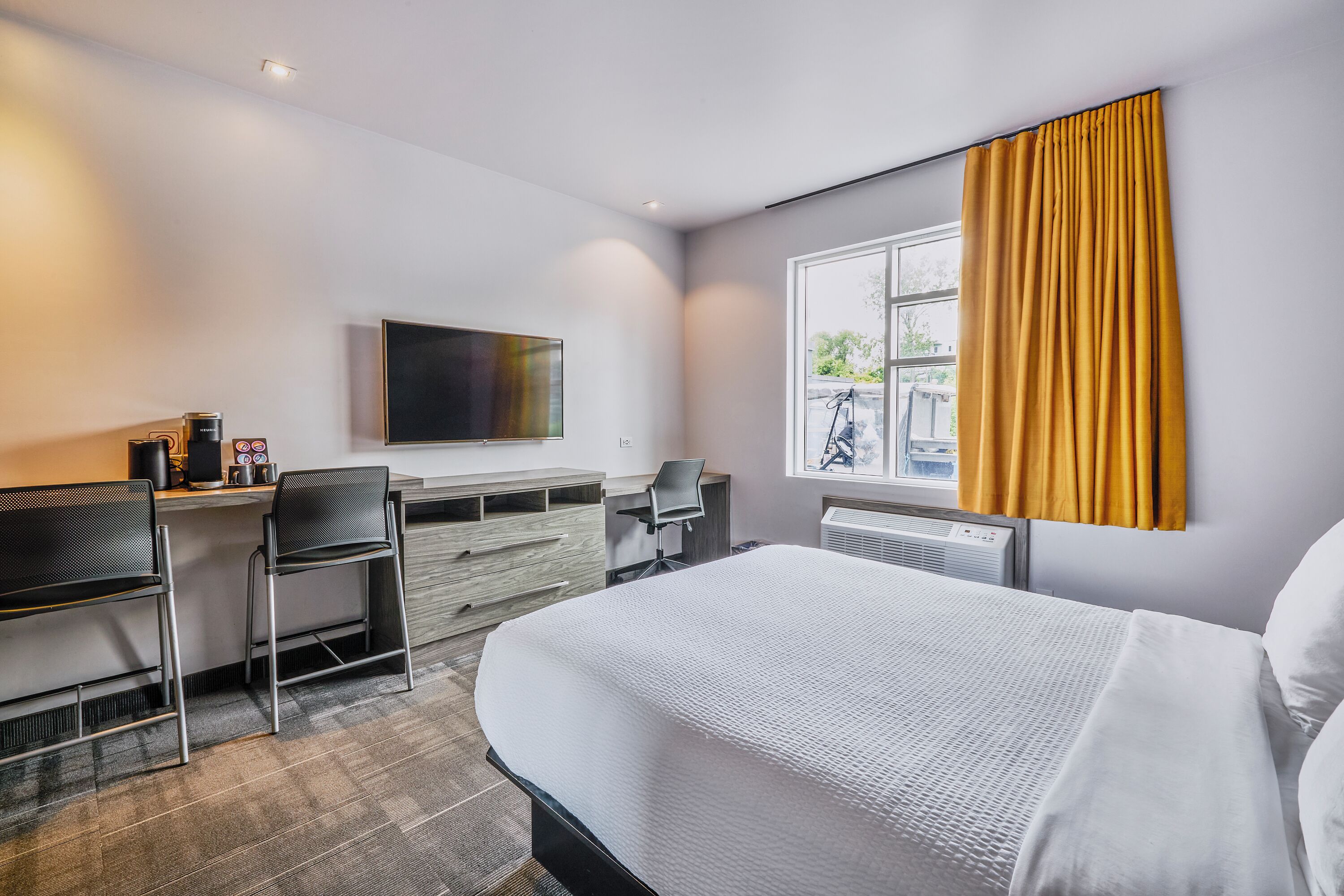 Habitación de hotel con cama, escritorio con silla, televisor y ventana con cortinas.