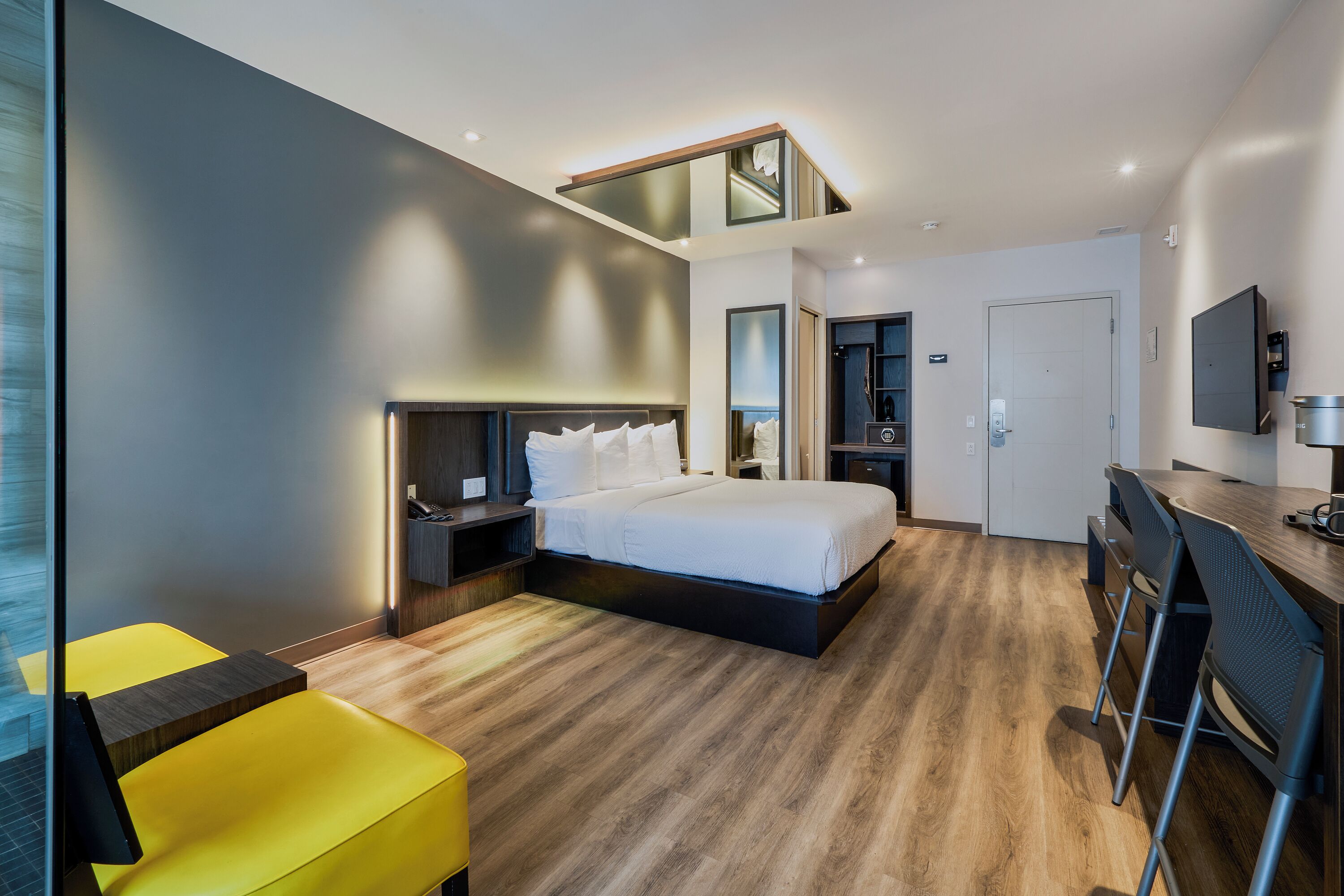 A modern hotel room with a bed, a desk, a chair, and a small seating area.