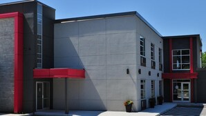 A modern building with a grey facade, red accents, and a parking lot. - Hôtel Ô Laval (Laval)