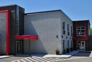 Un edificio moderno con fachada gris, detalles en rojo y un estacionamiento.