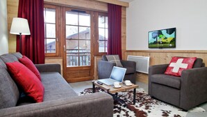 Ein Wohnzimmer mit Sofa, Sessel und einem Tisch mit Laptop und Tassen.