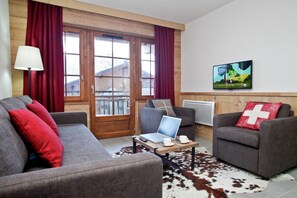 Ein Wohnzimmer mit Sofa, Sessel und einem Tisch mit Laptop und Tassen.