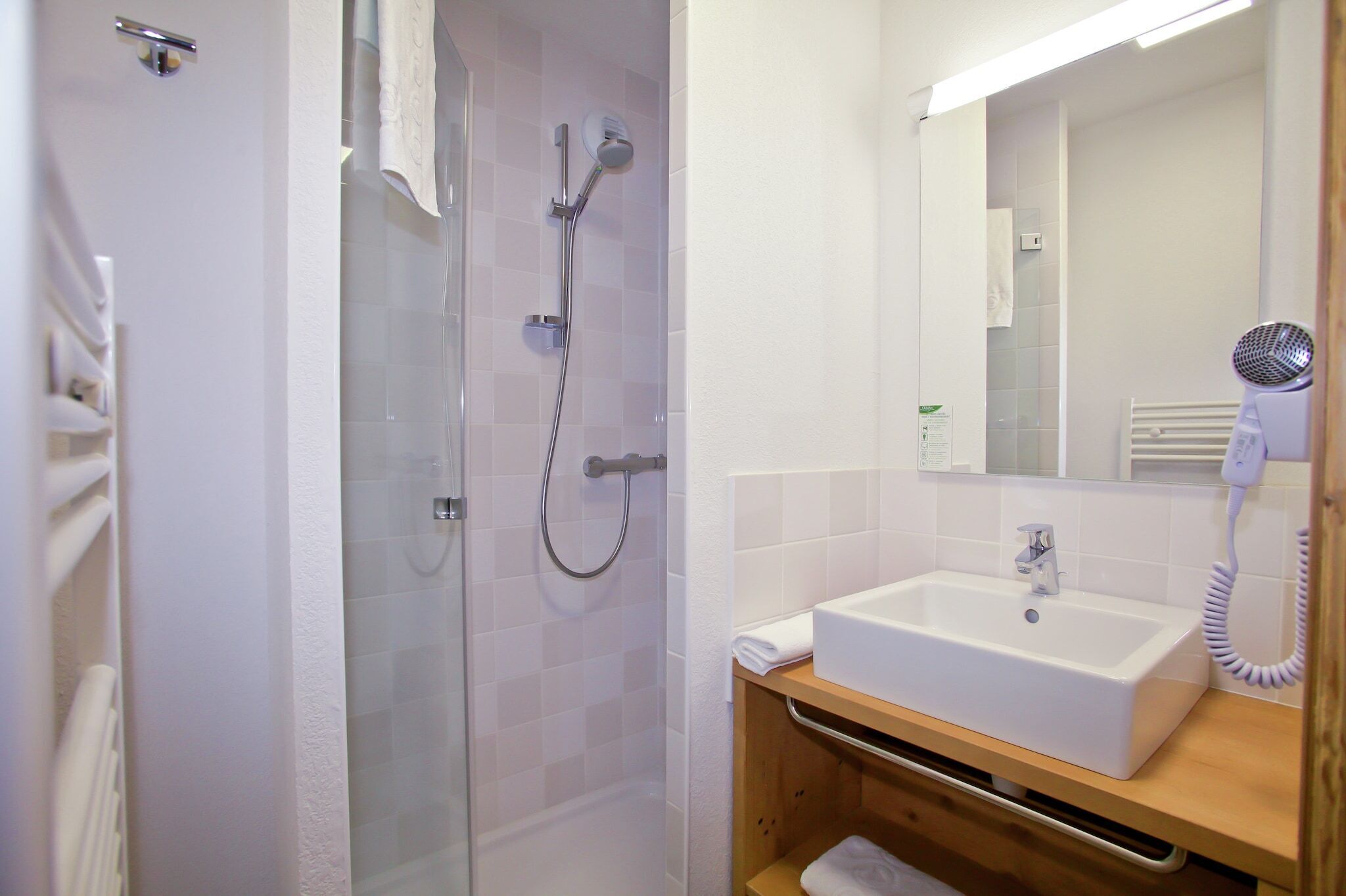 Une salle de bain avec une douche à parois de verre, un lavabo blanc et un sèche-cheveux posé sur le comptoir.