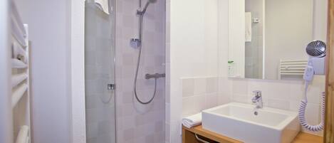Une salle de bain avec une douche à parois de verre, un lavabo blanc et un sèche-cheveux posé sur le comptoir.