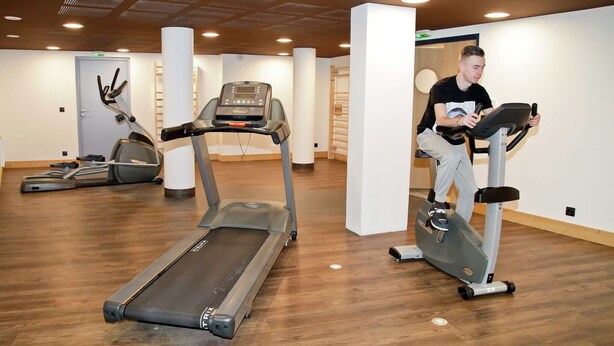 Ein Fitnessstudio mit Laufbändern und Crosstrainern, Holzboden und modernem Deckenbau.