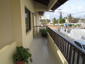 Varanda com planta em vaso, janela e vista para uma rua com edifícios e carros.
