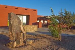A building with a modern design, featuring a large rock sculpture in the foreground, a stone wall, and a small tree. - Hopi Cultural Center (Second Mesa)
