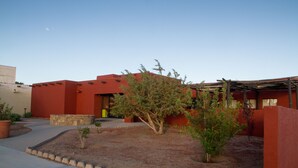 A building with a red exterior, a small garden with a tree, and a clear sky. - Hopi Cultural Center (Second Mesa)