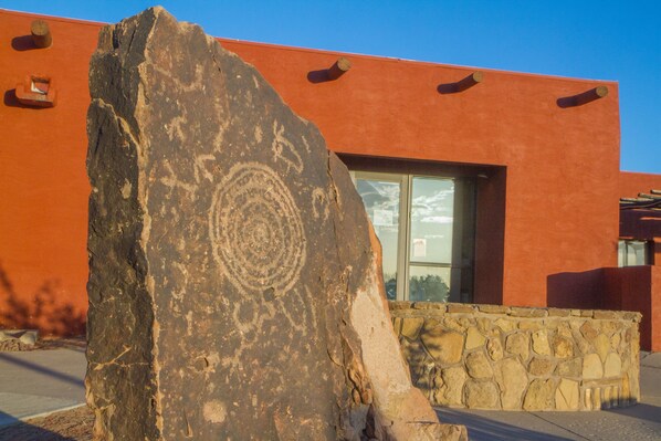 A large rock with carvings in front of a building with a red facade and a stone wall. - Hopi Cultural Center (Second Mesa)