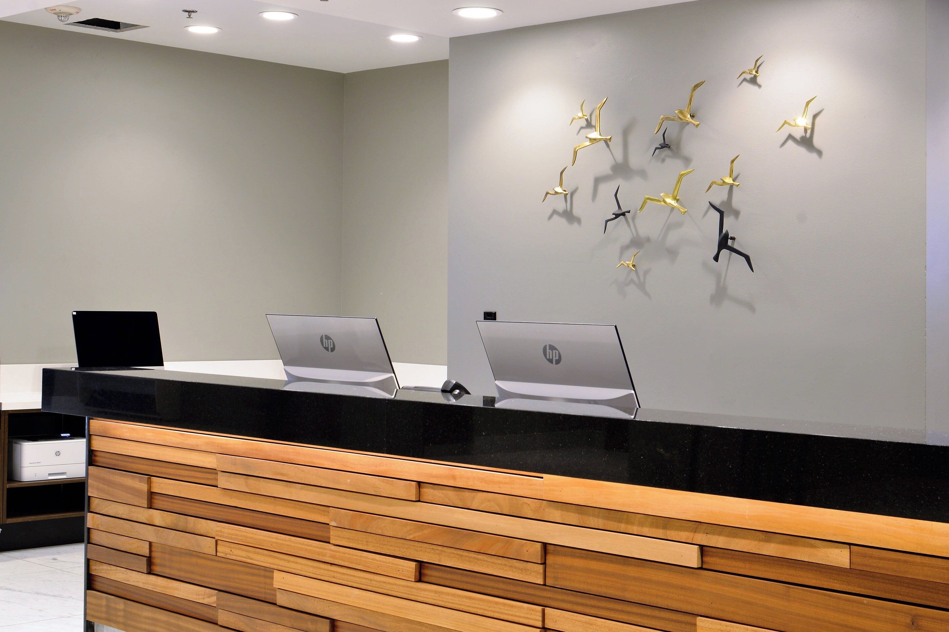 Un comptoir d’accueil avec deux ordinateurs portables HP, un panneau en bois et un mur orné de sculptures d’oiseaux.