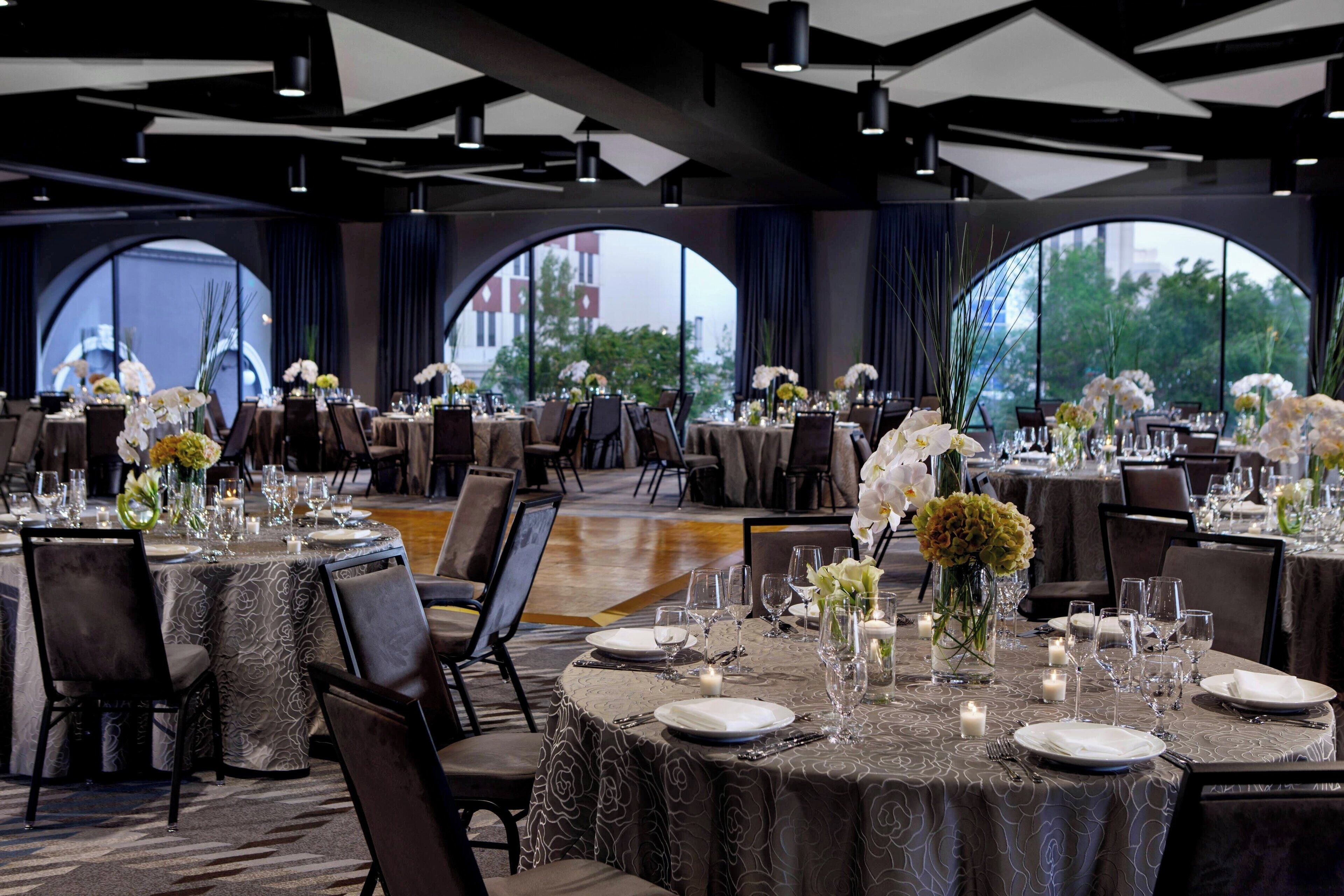 Un salón de banquetes con mesas redondas dispuestas para comer, con centros de mesa florales y velas.