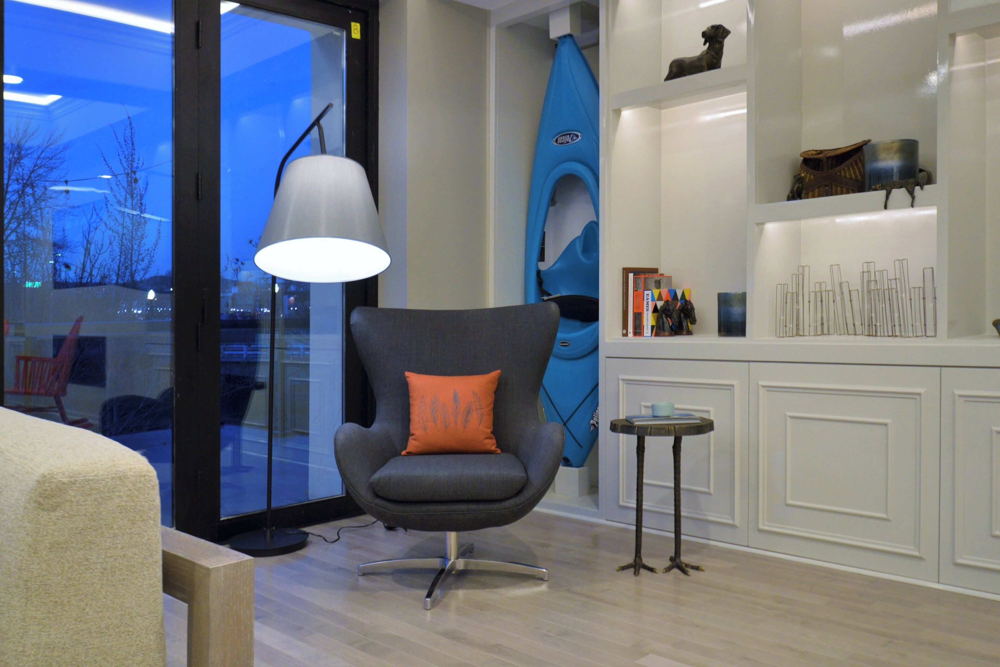 A modern room with a grey armchair, a blue kayak, and a white cabinet with decorative items.