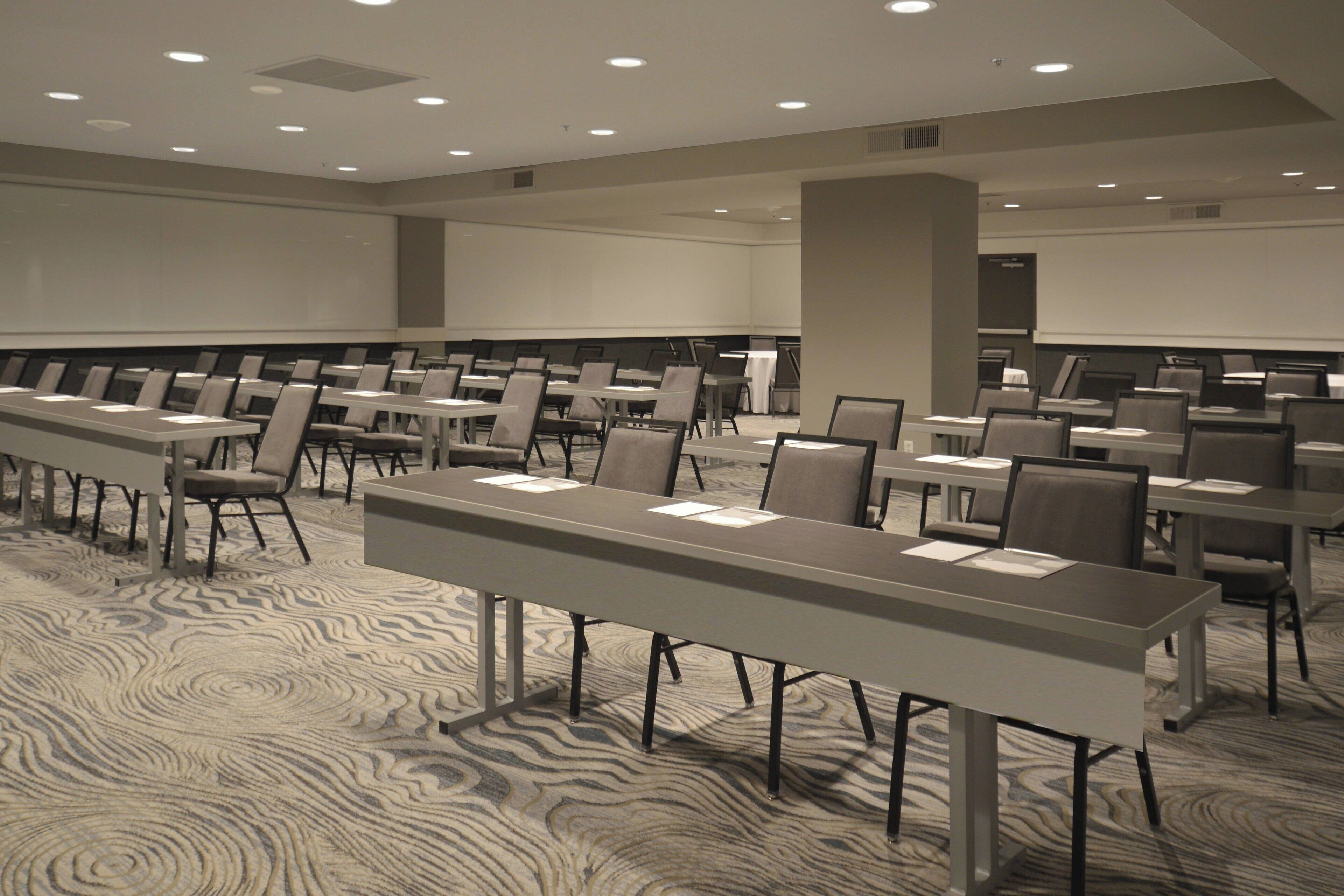 A conference room with multiple tables and chairs, a large screen, and a patterned carpet.