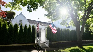 A white house with a porch, a staircase, and two American flags.