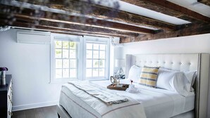 A bedroom with a large bed, wooden beams, a window, and a bedside table with a lamp.