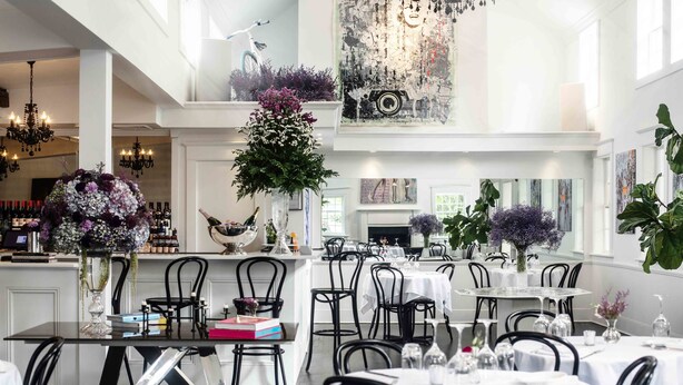 A spacious dining area with multiple tables and chairs, a bar area with bottles, and decorative plants.