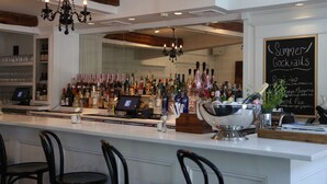 A bar area with a white countertop, multiple bottles of alcohol, a cash register, and a chalkboard menu listing summer cocktails.