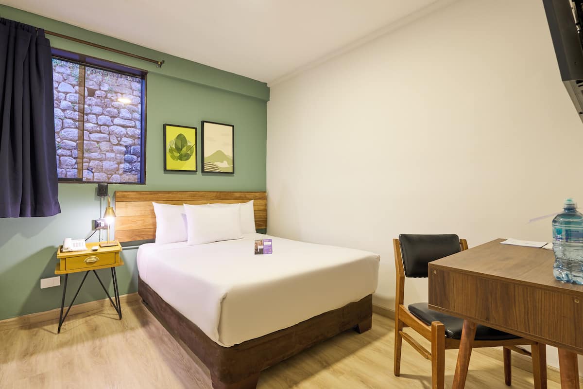 Une chambre d’hôtel bien rangée, avec un lit, une table de chevet, une lampe et une petite table sur laquelle se trouve une bouteille d’eau.