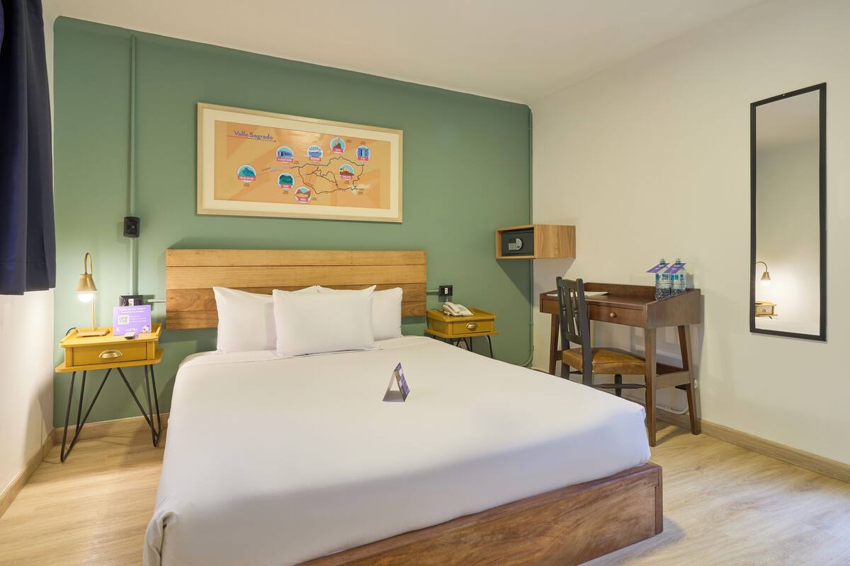 Une chambre d’hôtel avec un grand lit, un bureau, une chaise, une table de chevet et un téléviseur fixé au mur.