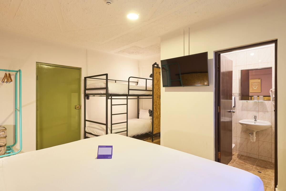 Une chambre avec des lits superposés, un lit simple, une salle de bain avec un lavabo et une porte verte.
