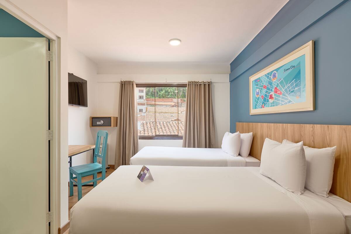 Une chambre d’hôtel avec deux lits, un bureau, une chaise et une fenêtre avec des rideaux.