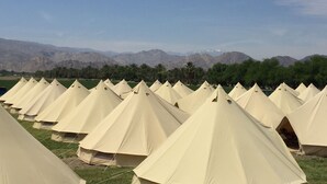 A row of beige tents arranged in a campsite with a mountainous backdrop.