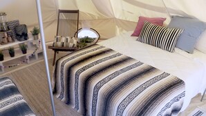 A tented room with a bed, pillows, a chair, and shelves with plants.