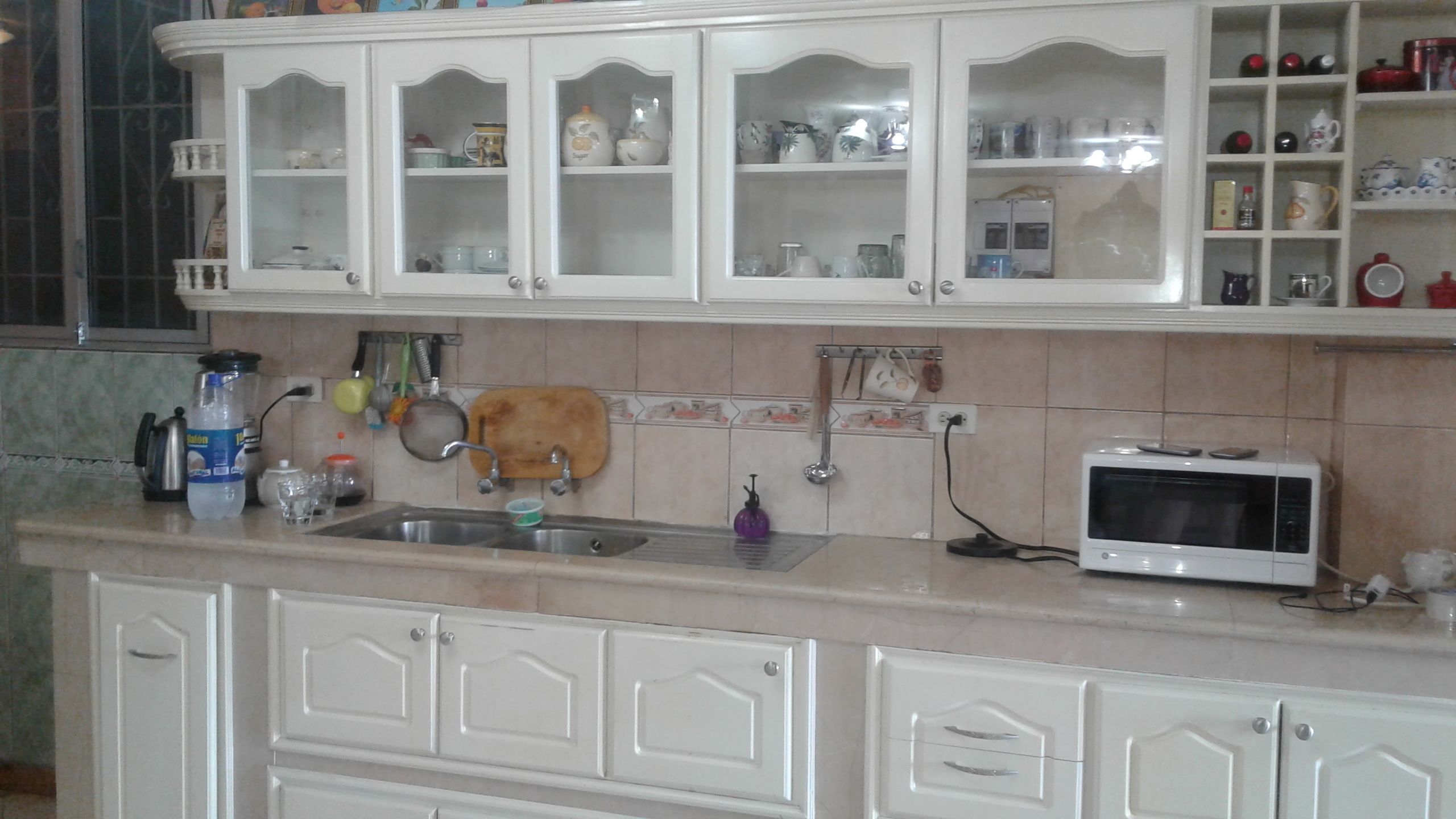 A kitchen with white cabinets, a sink, a microwave, and various kitchen utensils.