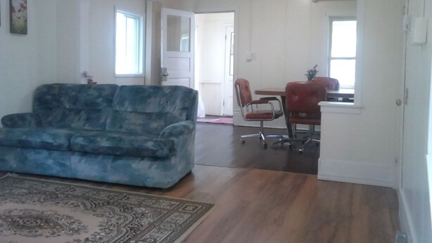 A living room with a blue sofa, a dining area with a table and chairs, and a kitchen visible through an archway. - Canora Home Rentals Holiday Cottage (Canora)